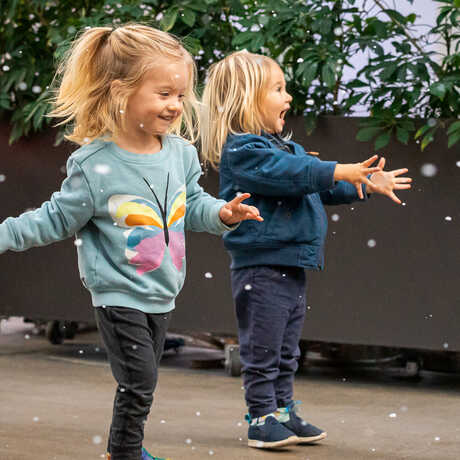 2 young girls joyfully frolic in the indoor snow flurries during Tis the Season for Science at the Academy