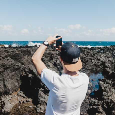 Man on rocky coastline takes picture with mobile phone