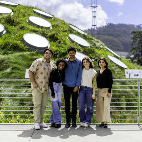 Five content creators stand against a railing on the Academy living roof, with a grassy hill in the background.