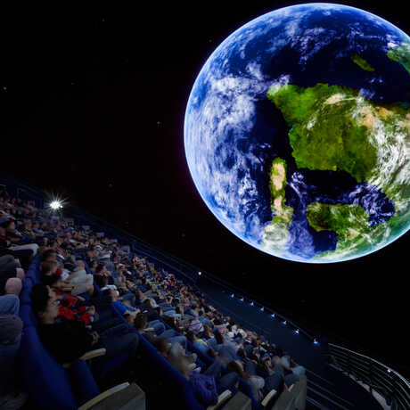 A shot from inside the planetarium of an audience looking at a giant planet Earth
